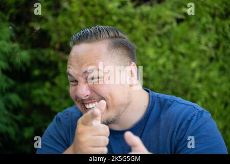 Mischievous happy young man pointing a finger at the camera with an impish grin outdoors in a garden Stock Photo