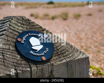 A black circular sign with white print and acorn logo affixed to a wooden post marks the way of the England Coast Path National Trail. Taken in Kent, Stock Photo