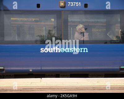 The side of a blue southeastern Railways carriage. Behind one of the two windows, commuters sit waiting for the train to continue its journey. Stock Photo