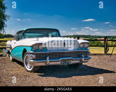 A 1958 door Buick sedan in turquoise and white. Parked in a rural setting on a sunny day with countryside in the background. Stock Photo