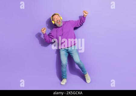 Photo of senior optimistic healthy man wear purple hoodie headphones dancing favorite songs tracks isolated on violet color background Stock Photo
