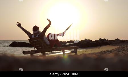 Santa Claus summer vacation. Santa Claus sunbathes. back view. Funny Santa, in flippers, is sitting on lounger, on beach by the sea and enjoying the sunset or sunrise, relaxing. at the seashore. High quality photo Stock Photo