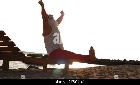 funny santa claus sunbathes. santa is sitting on wooden lounger on beach by the sea, relaxing, stroking his white beard, at sunrise. santa claus is on summer vacation, at the seashore. High quality photo Stock Photo