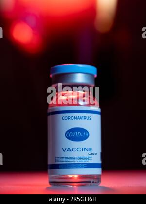 Coronavirus vaccine. Pandemic immunization. Flu inoculation. Covid-19 prevention. Dose vial glass bottle with blue label on black background with red Stock Photo