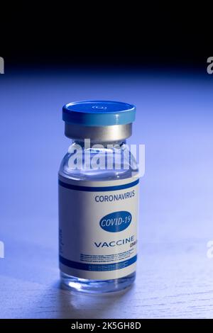 Covid-19 vaccine. Pandemic immunization. Coronavirus prevention. Flu inoculation. Dose vial glass bottle with label on defocused dark blue background. Stock Photo