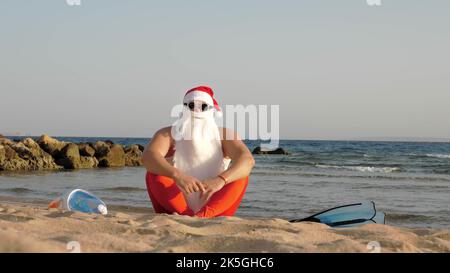 Santa Claus summer vacation. Father Christmas having fun. Santa doing yoga. Funny Santa, in sunglasses, with flippers and snorkeling mask, on beach by the sea. Santa going to snorkel. High quality photo Stock Photo