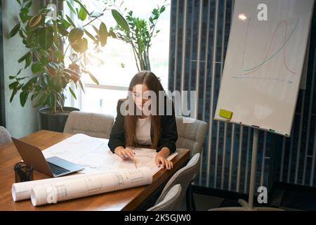 Design professional seated at office desk analyzing floor plan Stock Photo