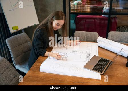 Pleased female architect analyzing rolled-out technical drawing Stock Photo