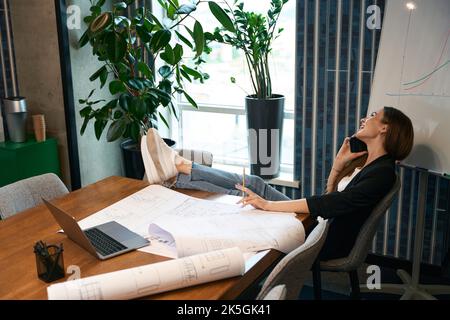 Smiling female architect with pencil in hand talking on smartphone Stock Photo