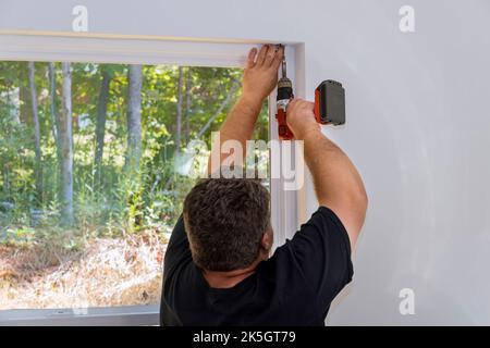 Contractor is screw the fastening to install blinds on windows of newly constructed home Stock Photo