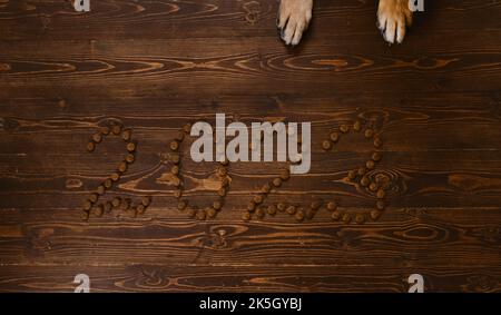The inscription 2023 is laid out with dog dry food on brown wooden background and red paws of german shepherd. Original creative Christmas layout for Stock Photo