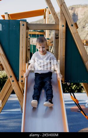 A vertical shot of a smiling boy going down the slide in a playground Stock Photo