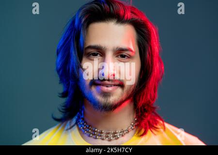 Attractive male portrait. Disco party. Trendy neon light people. Happy man yellow t-shirt beads necklace in blue red vibrant color glow isolated deep Stock Photo