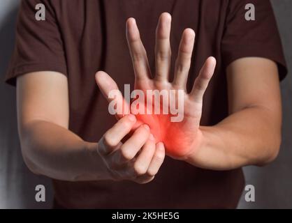 Asian young man scratching his hand. Concept of itchy skin diseases such as scabies, fungal infection, eczema, psoriasis, rash, allergy, etc. Stock Photo