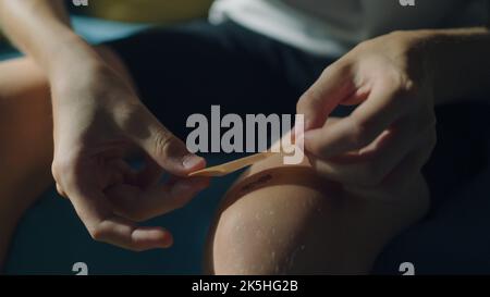 Teenage boy applying medical adhesive plaster on his knee. First aid after injury. Cuts, abrasions and lightly bleeding wounds while doing sports concept. Stock Photo