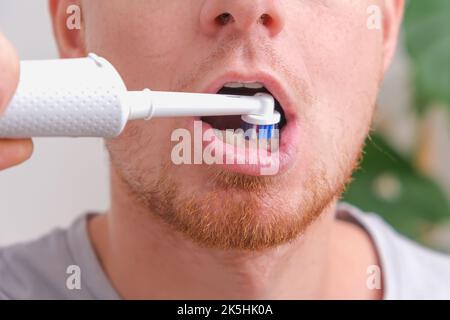A young man with red beard is brushing his teeth with a white electric brush. Oral care. Stock Photo