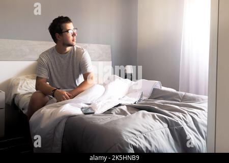 Portrait of a man sitting in bed looking out of the window Stock Photo