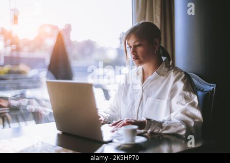 A portrait of a beautiful mature Hispanic female working with her laptop while sitting next to the window of a cafe; a plus-size cute Brazilian woman Stock Photo