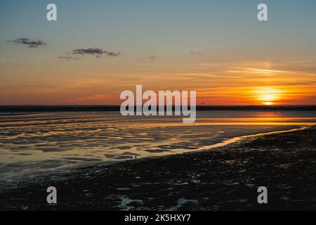 A beautiful sunset at low tide. The sand has a rippled texture and the water is catching the golden light. The view is from Ramsgate looking towards S Stock Photo