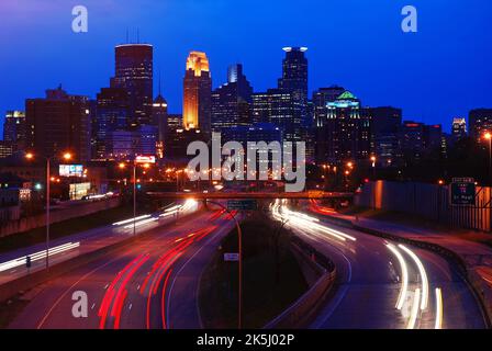 Traffic moves to and from the downtown skyline of Minneapolis, Minnesota, traveling along the interstate highway to the city center at night Stock Photo