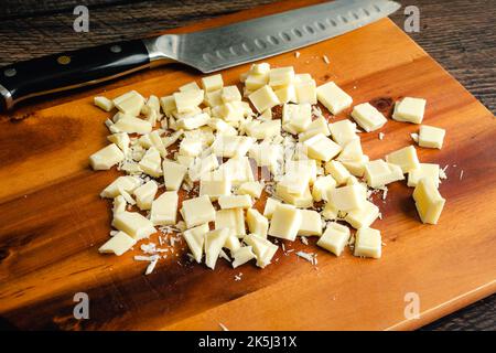 Chopped White Chocolate on a Wood Cutting Board: Pieces of white chocolate with a kitchen knife on a wooden carving board Stock Photo
