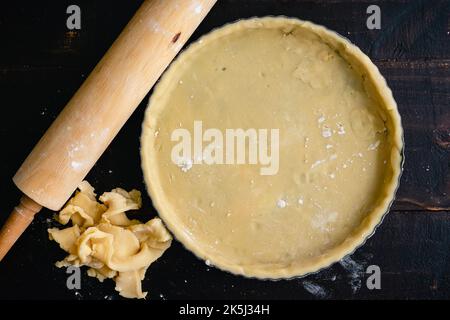 Tart Pan Filled with Raw Pastry Dough: Dough-filled tart pan with pastry crust scraps and a rolling pin Stock Photo
