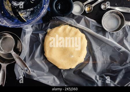 Tart Crust Dough on a Piece of Plastic Wrap: Raw pastry dough formed into a disk shape surrounded by kitchen utensils Stock Photo
