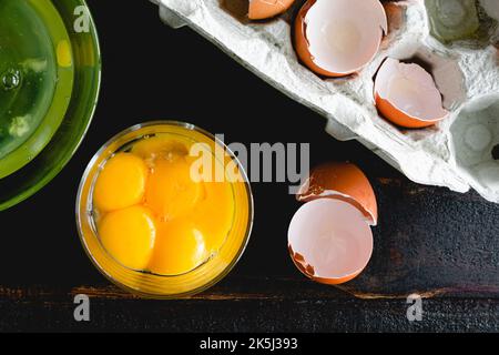 Separated Egg Yolks in a Glass Bowl on a Wooden Table: Egg yolks, egg whites, and egg shells on a dark wood background Stock Photo