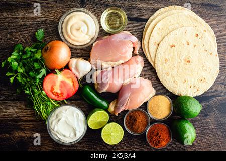 Raw Ingredients for Grilled Chicken Tacos and Pico de Gallo: Chicken thighs, flour tortillas, and other taco ingredients viewed from above Stock Photo