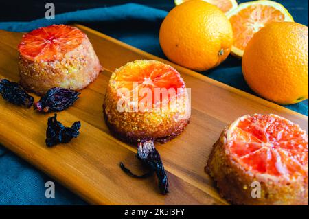 Upside Down Blood Orange, Hibiscus and Polenta Cakes on a Wood Cutting Board: Mini cakes soaked in blood orange syrup and topped with a hibiscus glaze Stock Photo