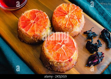 Upside Down Blood Orange, Hibiscus and Polenta Cakes on a Wood Cutting Board: Mini cakes soaked in blood orange syrup and topped with a hibiscus glaze Stock Photo