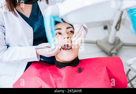 Top view of dentist doing cleaning to female patient lying down. Dentist doctor examining mouth to patient lying on chair, Female dentist examining Stock Photo
