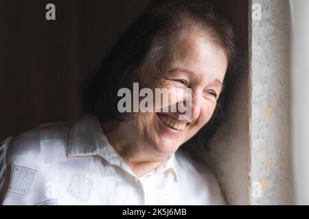 Elderly woman standing and looking through the window Stock Photo