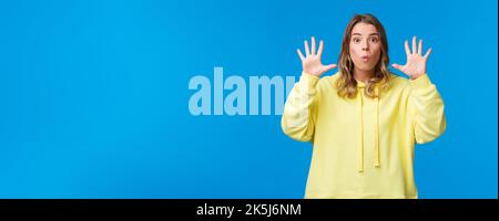 Imagine this. Excited and happy outgoing blond girl explain something and gesturing, holding hands near face, showing number ten, talking to camera Stock Photo