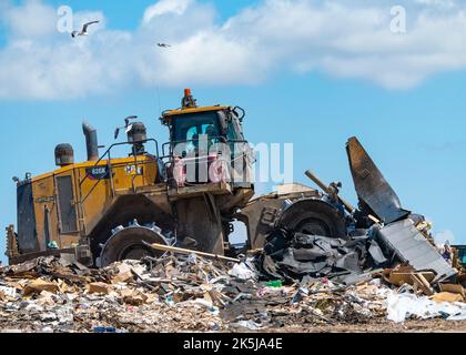 Giant bulldozer pushing piles of trash on top of landfill under sunny sky. Stock Photo