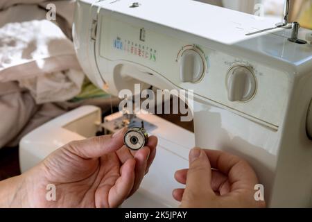Using sewing machine, seamstress puts threads from metal spools into machine Stock Photo
