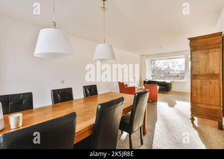 Comfortable chairs and wooden table placed under stylish lamps against wall with cupboard in dining room Stock Photo
