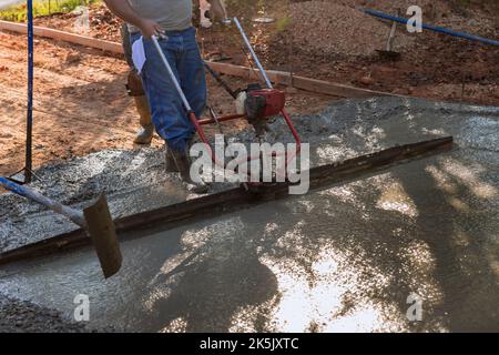 Machine is used to align compacted layer fresh concrete on new driveway that has been constructed Stock Photo