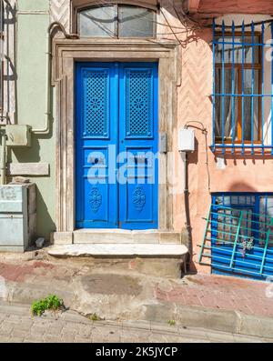 Exterior shot of blue painted decorated metal door beside wrought iron window, in a colorful stone wall painted in orange and green, on city street Stock Photo