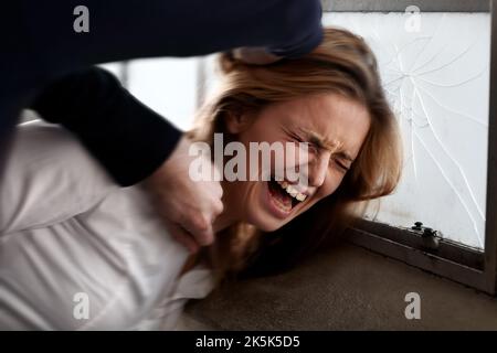 Act of violence. Abused young woman with her head being smashed against a window by an attacker. Stock Photo