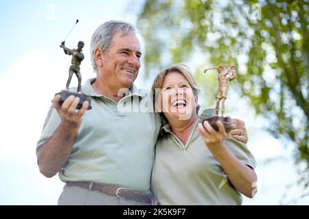 Champions of golf. Low angle view of a mature couple laughing and smiling with their golfing trophies. Stock Photo
