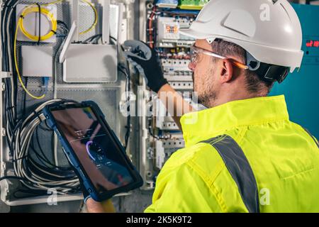 Man, an electrical technician working in a switchboard with fuses, uses a tablet. Stock Photo