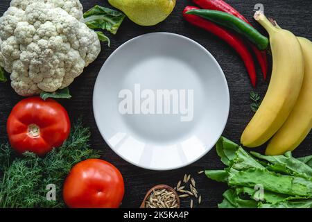 Vegetables on black background, flat lay composition with empty plate. Stock Photo
