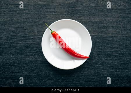 Flat lay, chili peppers on a white plate on a black background. Stock Photo
