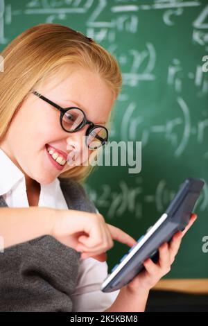 Calculators make maths fun. A cute blonde girl using a calculator in maths class. Stock Photo