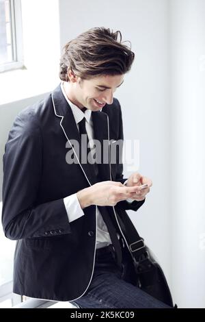Taking a minute to send a text. A young man typing a message on his cellphone. Stock Photo