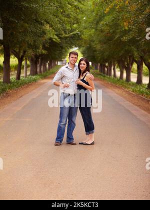 They have walked a long road together. Portrait of a young wine maker standing in the road with his young wife. Stock Photo