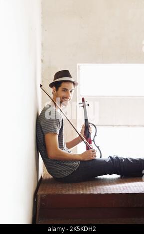 Hes ready to play anywhere, anytime. Handsome young musician holding his violin on a stairwell. Stock Photo