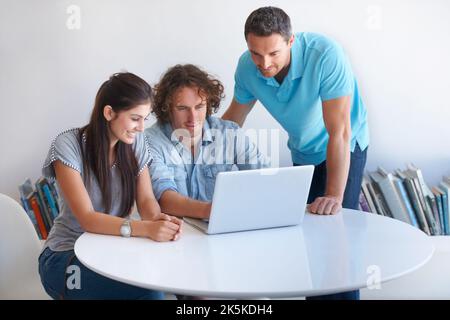Focused on the task at hand. three coworkers gathered around a laptop in the office. Stock Photo