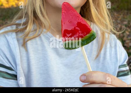 Girl eating a lollipop. Young woman holding a red candy watermelon lollipop in hand. Close up. Selective focus Stock Photo